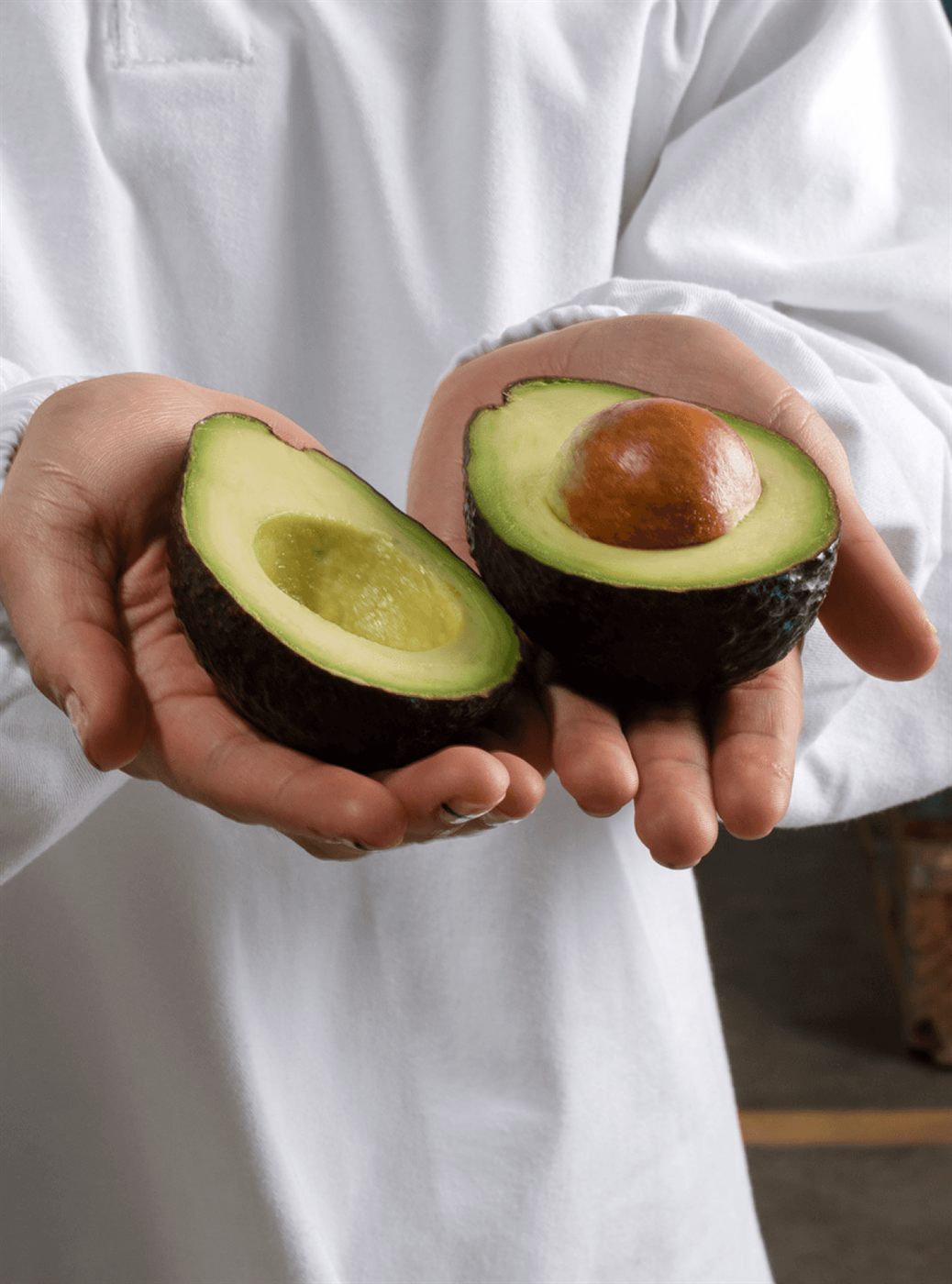 Two open halves of a Hass avocado held in both hands
