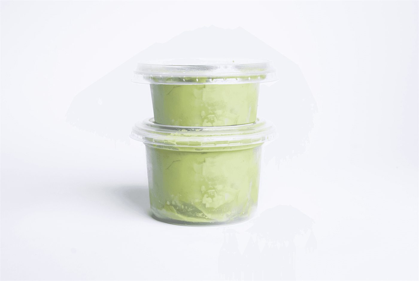 Two unbranded cups of guacamole stacked on a white surface