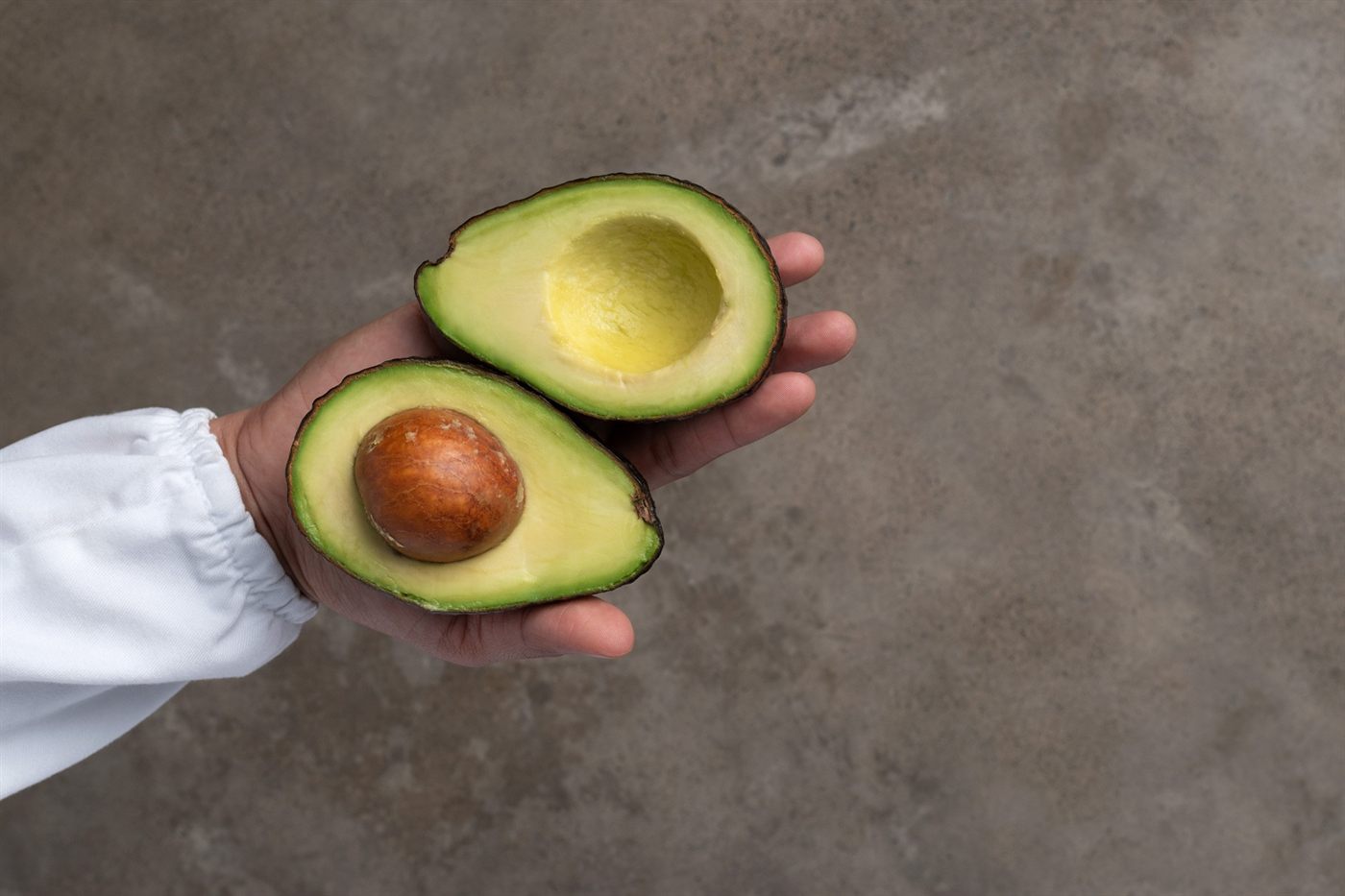 A hand holding a Hass avocado cut in half, stone still in place